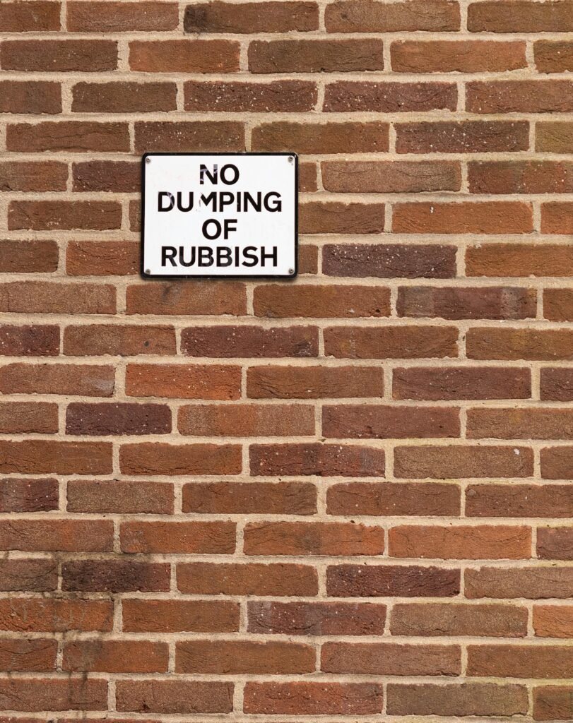 A street-facing brick wall with a 'No Dumping Of Rubbish' sign prominently displayed.